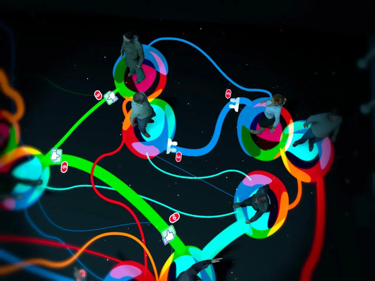 Dark projected visualization of glowing green, cyan, red and orange curving lines linking bright circular nodes with small figures and icons.