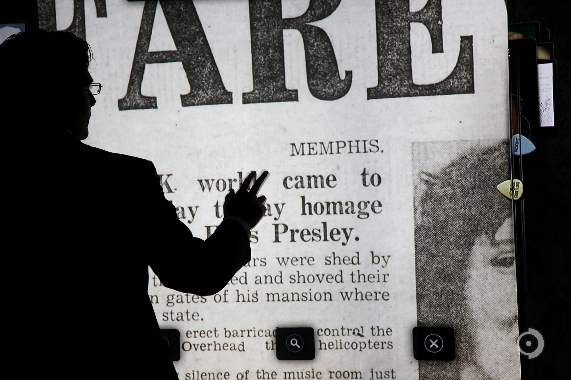 Silhouette of a person raising a hand toward a large projected newspaper page about Memphis and Presley with a portrait photo.