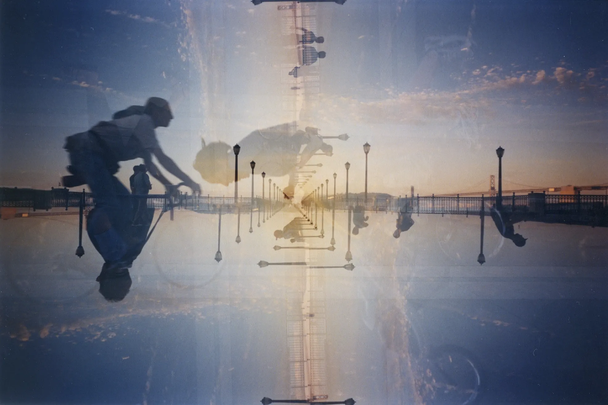 Mirrored double-exposure photograph of a waterfront promenade with lampposts, silhouetted figures, and sunset sky.